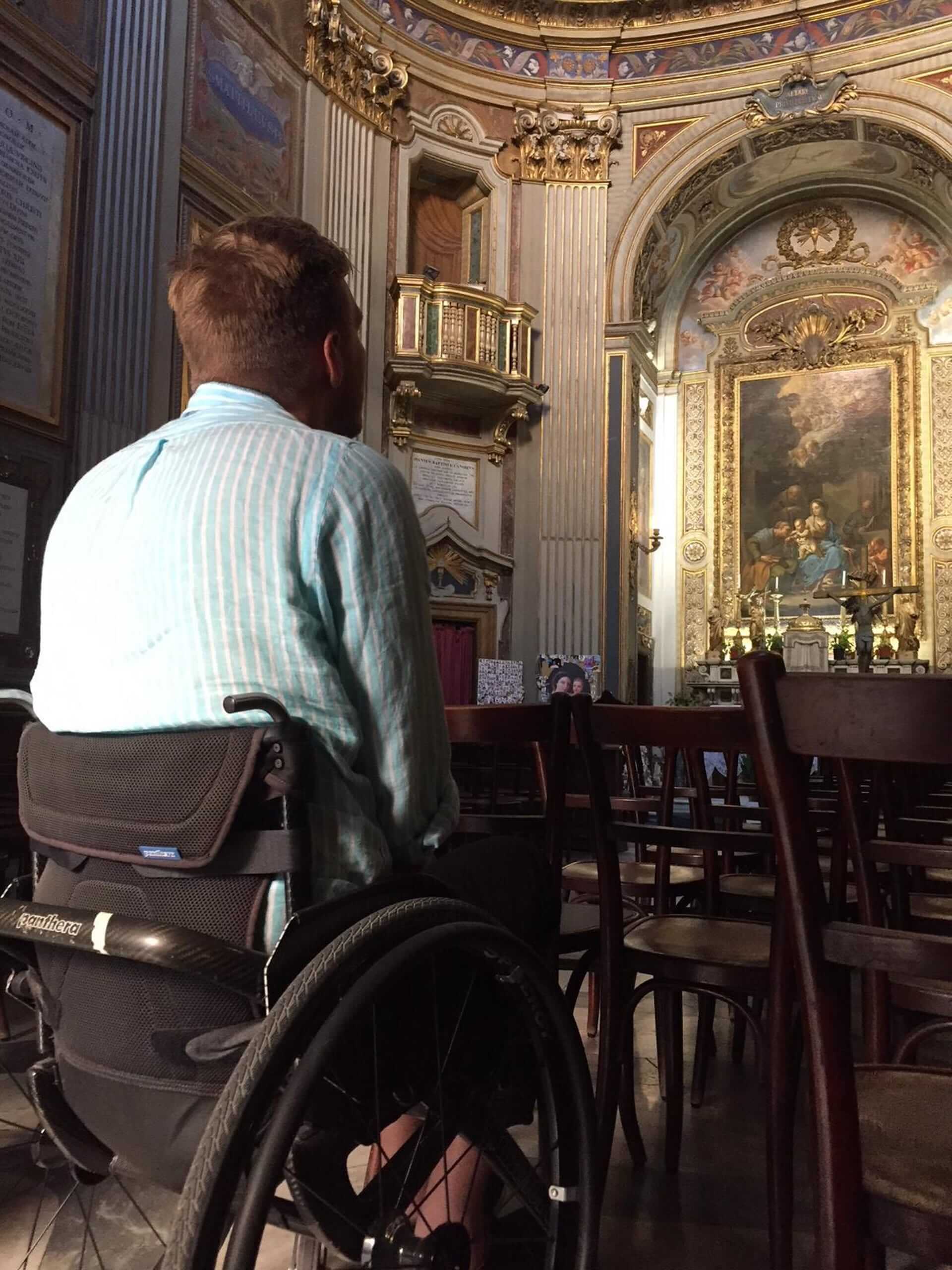 Bilde av artikkelskribent i rullestol inne i en kirke. Han sitter med ryggen til kameraet og kikker mot alteret. Han er alene.